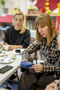 Osoba niewidoma trzymająca w ręce sprzęt do słuchania książek. W tle osoba przygląda się sytuacji