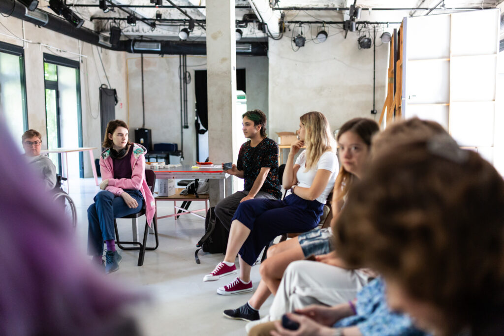 Uczestnicy projektu w czasie warsztatów siedzą w kółku na krzesłach.