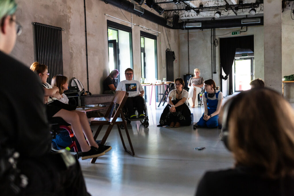 Uczestnicy projektu w czasie warsztatów siedzą w kółku na krzesłach, wózkach lub na podłodze