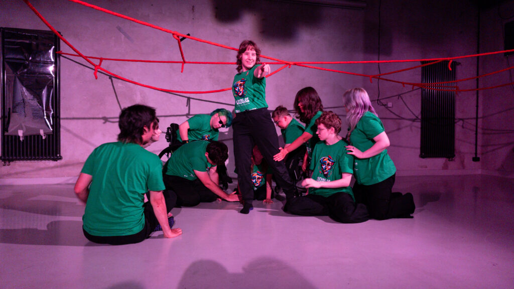 Scena w czasie spektaklu. Uczestnicy patrzą na młodą kobietę wskazującą palcem na przed siebie