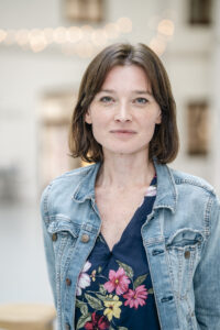 Uśmiechnięta brunetka z włosami do ramion w koszulce z kwiatami i w dżinsowej kurtce